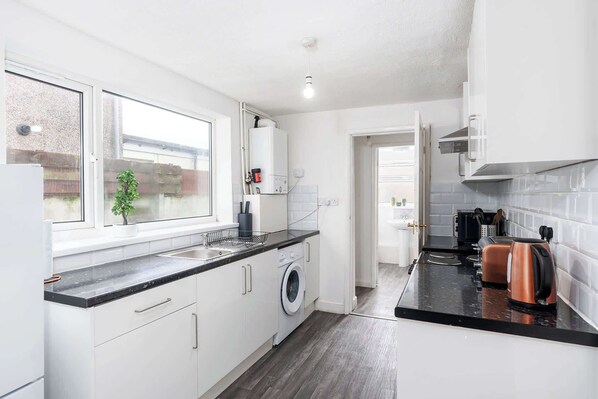 Kitchen with sink, washing machine, and coffee maker, offering a view of the outside.