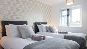 A hotel room with two beds, a patterned wall, a window with curtains, and a hanging light fixture. - Charming Liverpool House | Garden & Comfort (Liverpool)