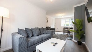 A modern living room with a grey striped sofa, a white coffee table, and a potted plant. - Charming Liverpool House | Garden & Comfort (Liverpool)