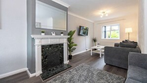 A living room with a fireplace, a sofa, a TV, and a window. - Charming Liverpool House | Garden & Comfort (Liverpool)
