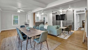 A spacious living area with a dining table, sofas, and a kitchen in the background.