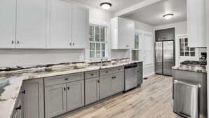 A modern kitchen with grey cabinets, stainless steel appliances, and a marble countertop.