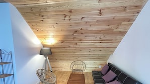 A loft-style room with a sloped ceiling, wooden flooring, a sofa with cushions, a coffee table, two chairs, and a floor lamp.