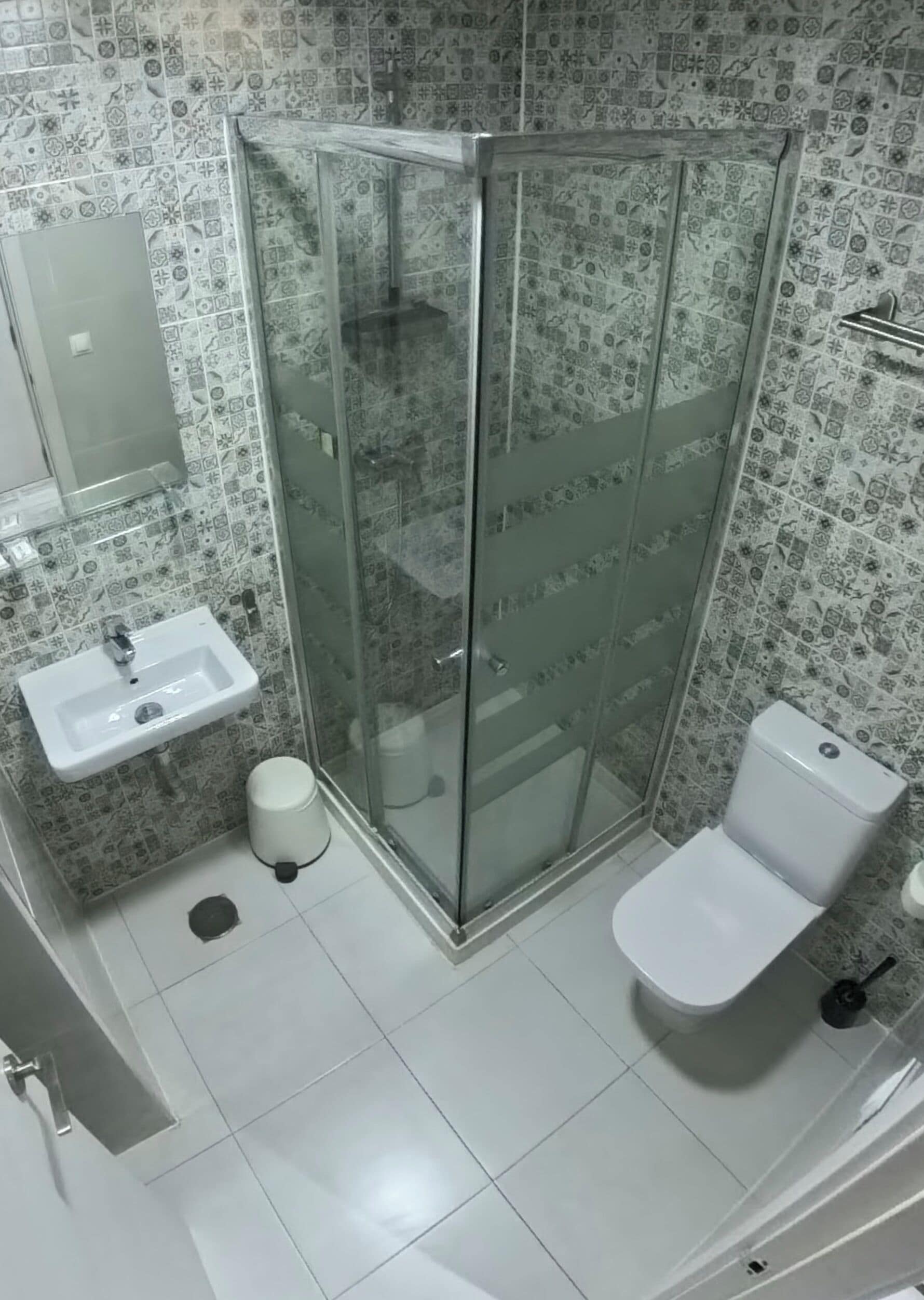 Un baño con ducha de vidrio, lavamanos, inodoro y azulejos decorativos en las paredes.