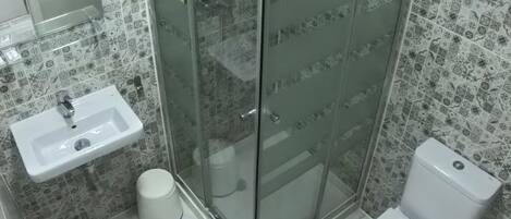 A bathroom with a glass-enclosed shower, a sink, a toilet, and patterned tiles on the walls.