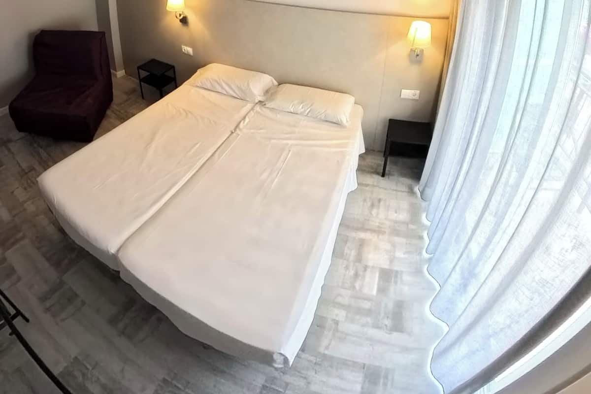 A hotel room with a large bed, two bedside tables, a chair, and a window with curtains.