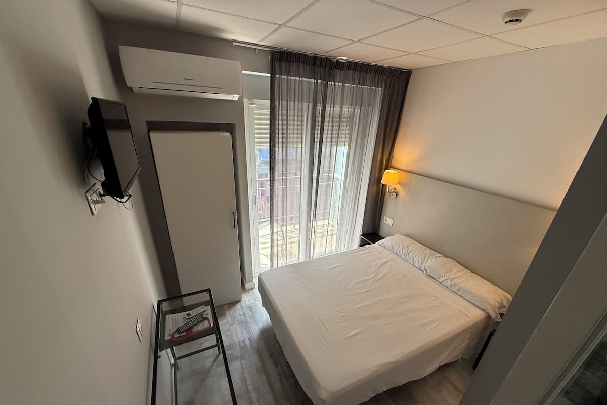 A hotel room with a bed, a desk with a lamp, a wardrobe, and a window with curtains.