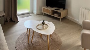 A modern living room with a flat-screen TV, a round table, and a woven ceiling light fixture. - Charm in the heart of the village: house with sunny garden close to the sea (Arradon)