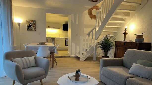 A modern living room with a sofa, armchair, and coffee table. A staircase leads to an upper level. - Charm in the heart of the village: house with sunny garden close to the sea (Arradon)