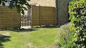 A stone building with a wooden gate, a small window, and a grassy yard. - Charm in the heart of the village: house with sunny garden close to the sea (Arradon)