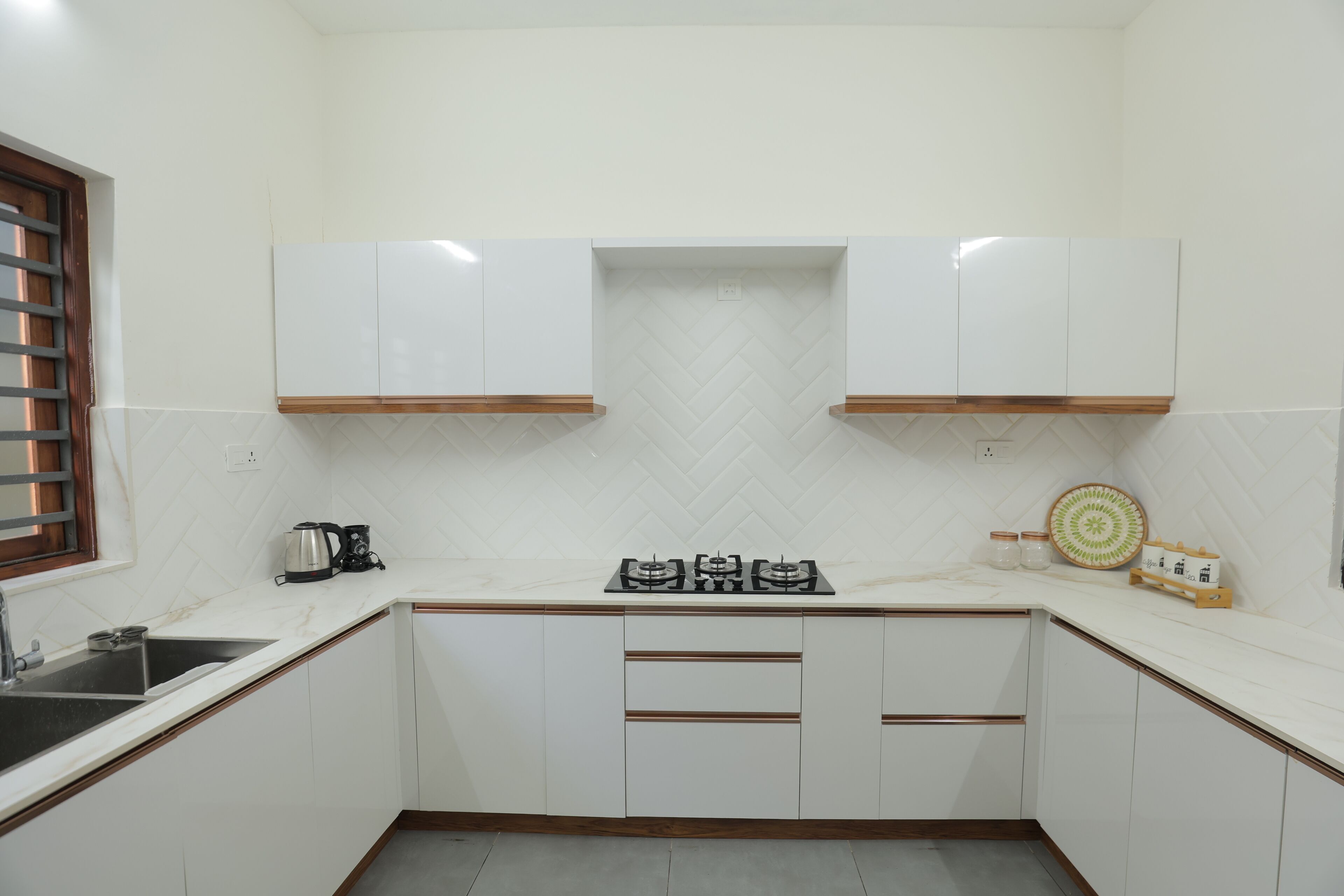 A kitchen with white cabinets, a gas stove, a coffee maker, and a window with blinds.