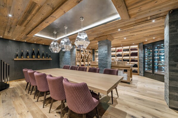 A modern dining area with a long wooden table, pink upholstered chairs, and hexagonal pendant lights. - Gourmet & Wine Hotel Austria 4s (Obergurgl)