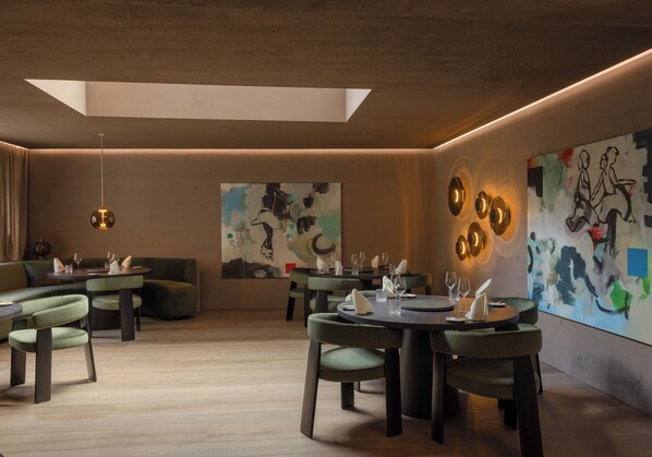 A modern dining area with round tables, green upholstered seating, and abstract art on the walls.
