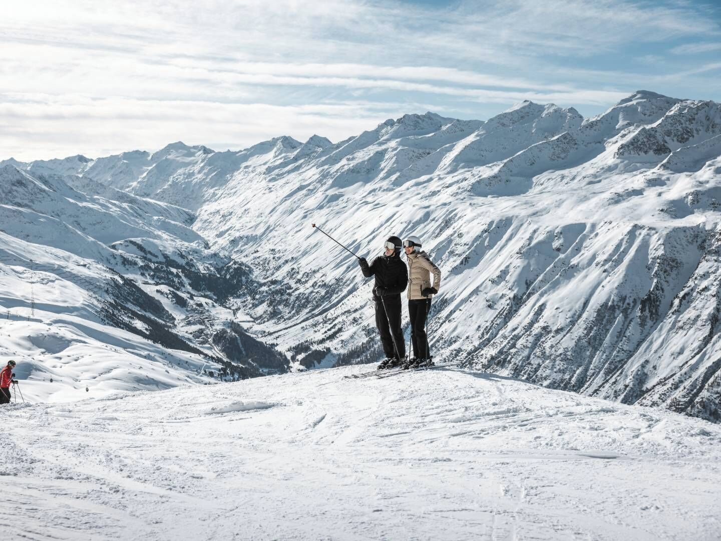 A snowy mountain landscape with two skiers standing on a ridge.