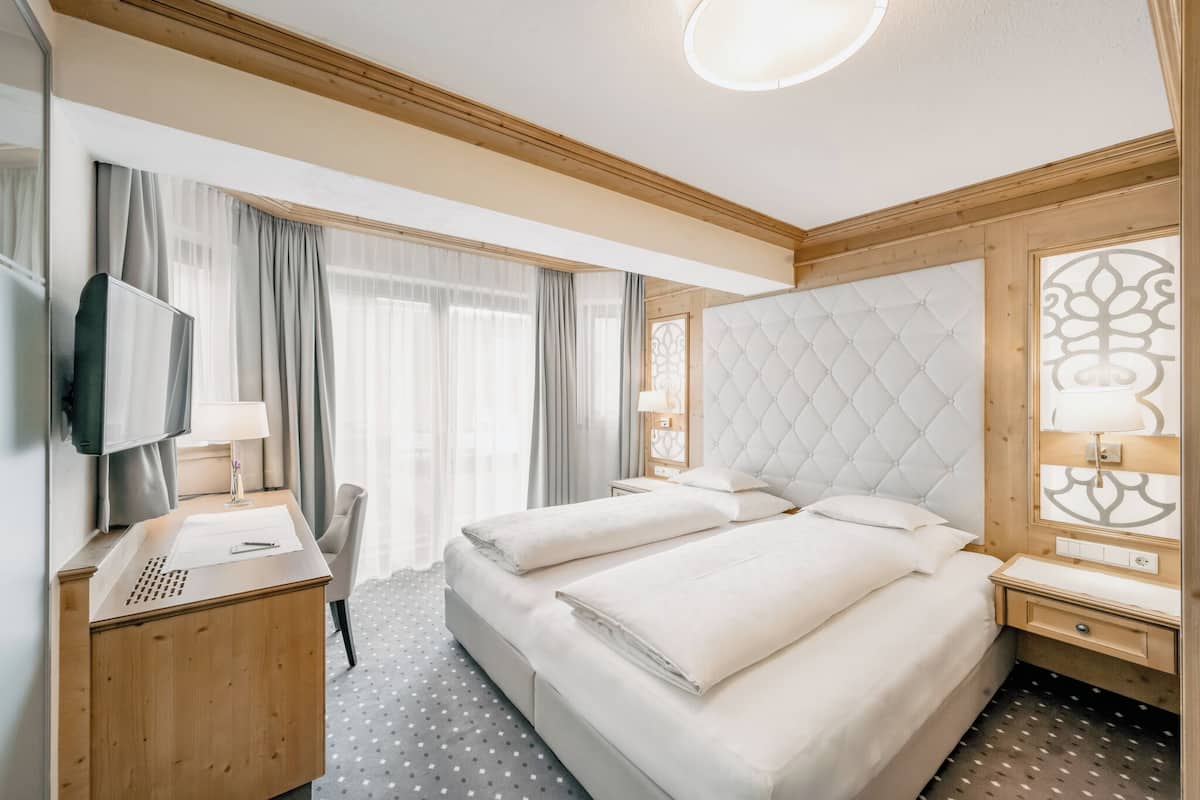 Habitación de hotel con dos camas, un escritorio, televisor y un amplio ventanal con cortinas.