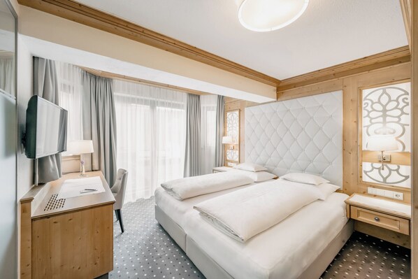 Habitación de hotel con dos camas, un escritorio, televisor y un amplio ventanal con cortinas.