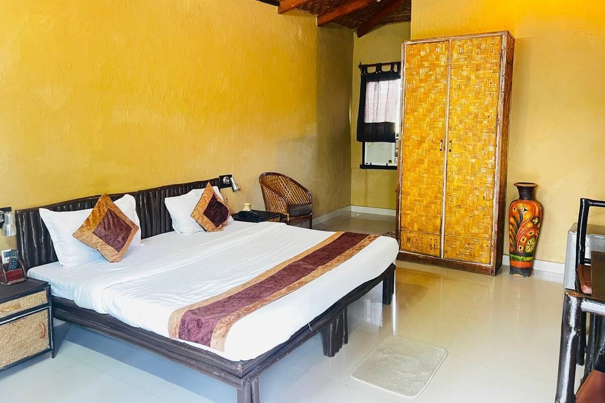 A hotel room with a large bed, a wooden headboard, a woven wardrobe, and a decorative vase.