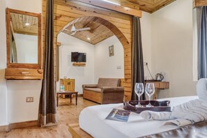 A hotel room with a bed, a wooden arched doorway, a television, a sofa, and a tray with glasses. - Ashoka Tiger Trail By VistaLux (Ramnagar)