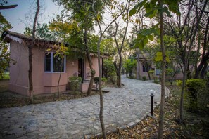 A stone-paved courtyard with a pink building, surrounded by trees and shrubs. - Ashoka Tiger Trail By VistaLux (Ramnagar)