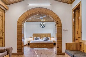 A bedroom with a wooden ceiling, a bed with a headboard, two bedside tables, and a wall-mounted clock. - Ashoka Tiger Trail By VistaLux (Ramnagar)