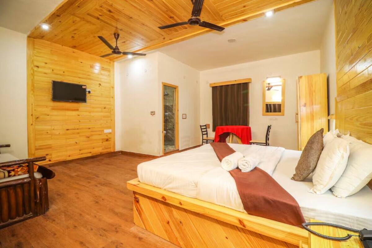 A wooden-paneled room with a bed, a TV mounted on the wall, and a ceiling fan.