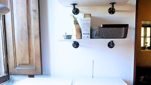Dos lavadoras de carga frontal en un cuarto de lavado con un armario de madera y un estante superior con diversos objetos.