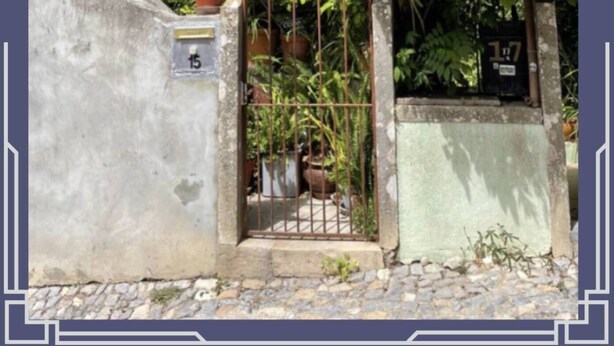 Un edificio con fachada de piedra, una reja de metal y un pequeño jardín con plantas en macetas.