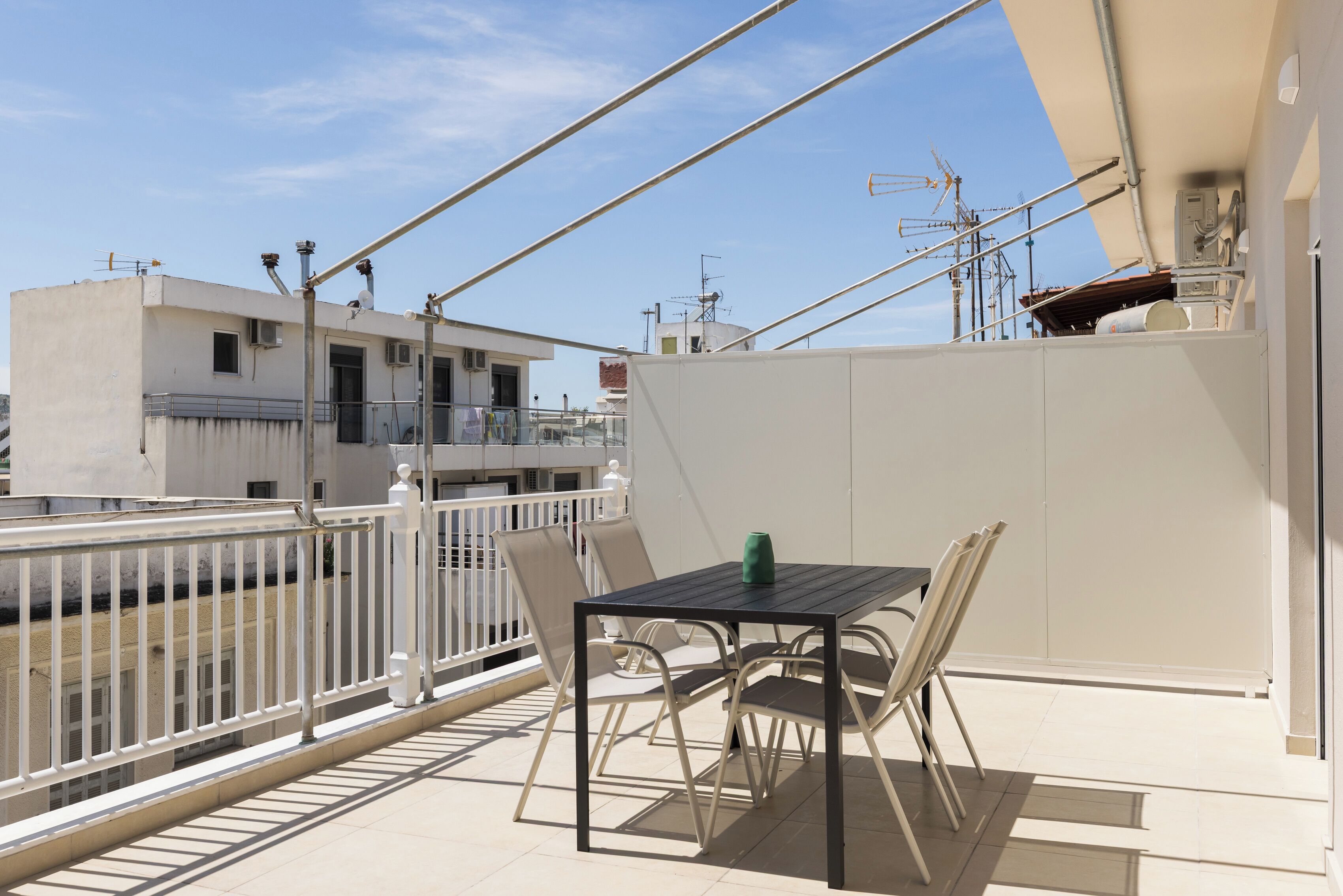 Un balcon avec une table et des chaises, une balustrade et une vue sur les bâtiments en arrière-plan.