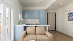 A modern kitchen with blue cabinets, a white countertop, and a beige sofa in a bright room with wooden flooring. - Celine Volos by halu! (Volos)