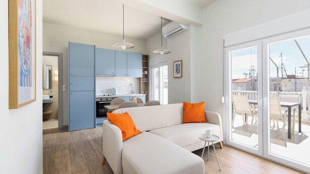A modern living room with a white sofa, orange cushions, and a small round table. - Celine Volos by halu! (Volos)