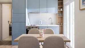 A compact kitchen with light blue cabinets, a wooden dining table, and chairs. - Celine Volos by halu! (Volos)