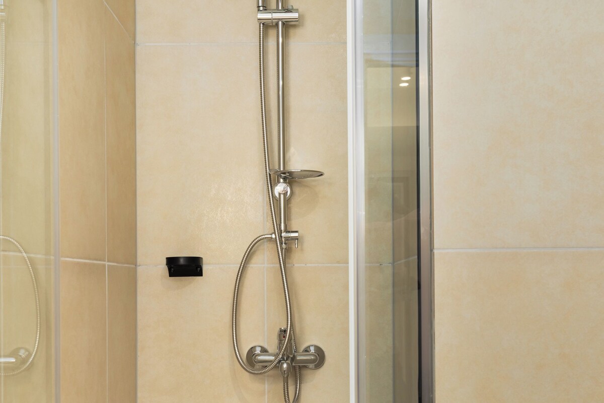 Ein modernes Badezimmer mit einer gläsernen Duschkabine, beigen Fliesen und einer sichtbaren Bedienkonsole.