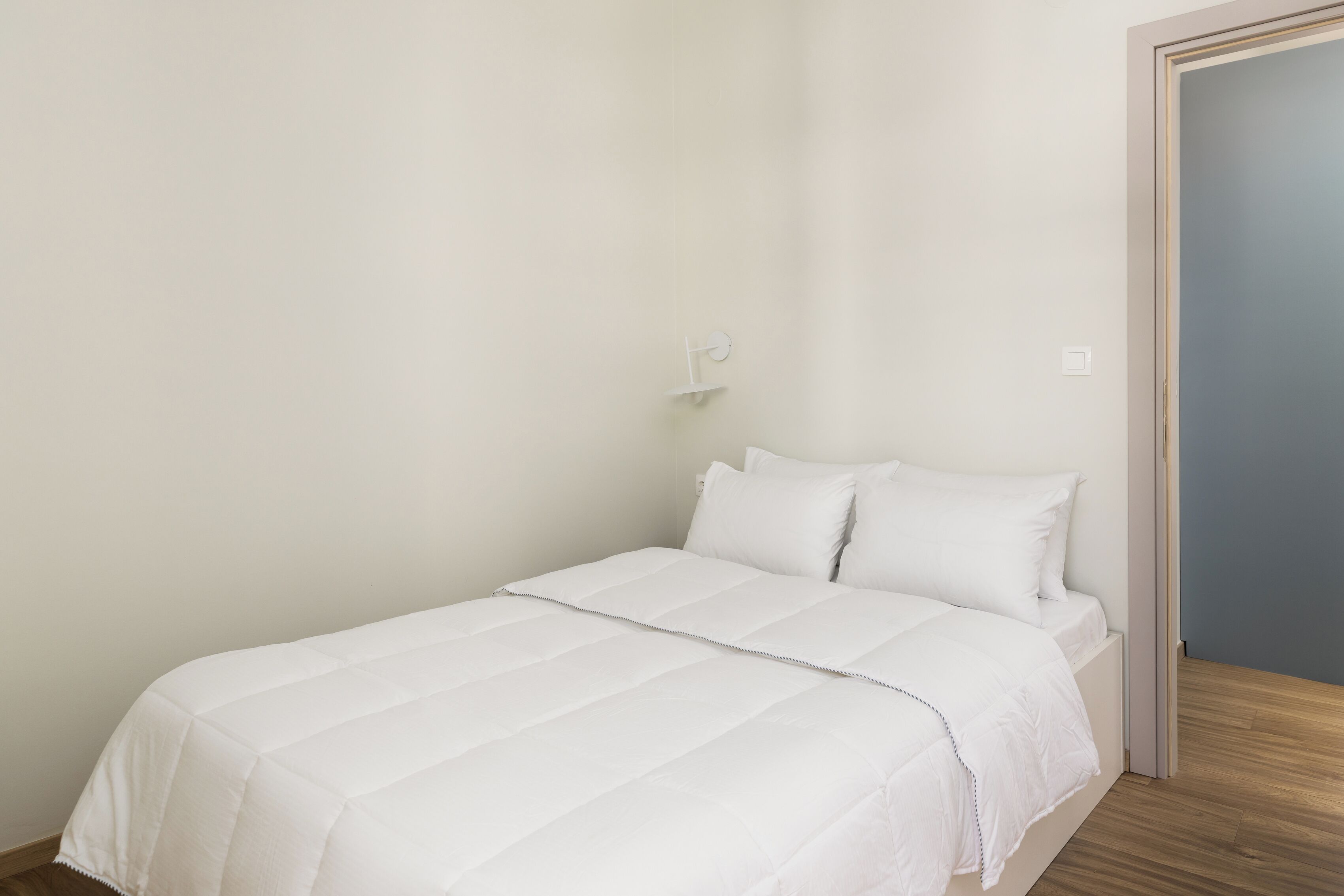A single bed with a white duvet in a room with a wooden floor and a plain white wall.