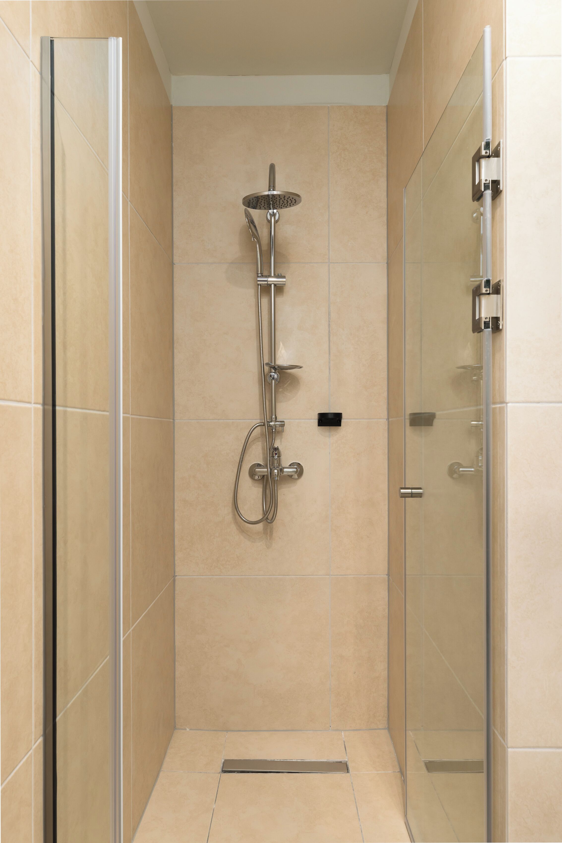 A modern shower area with a glass enclosure, a handheld showerhead, and a wall-mounted faucet.