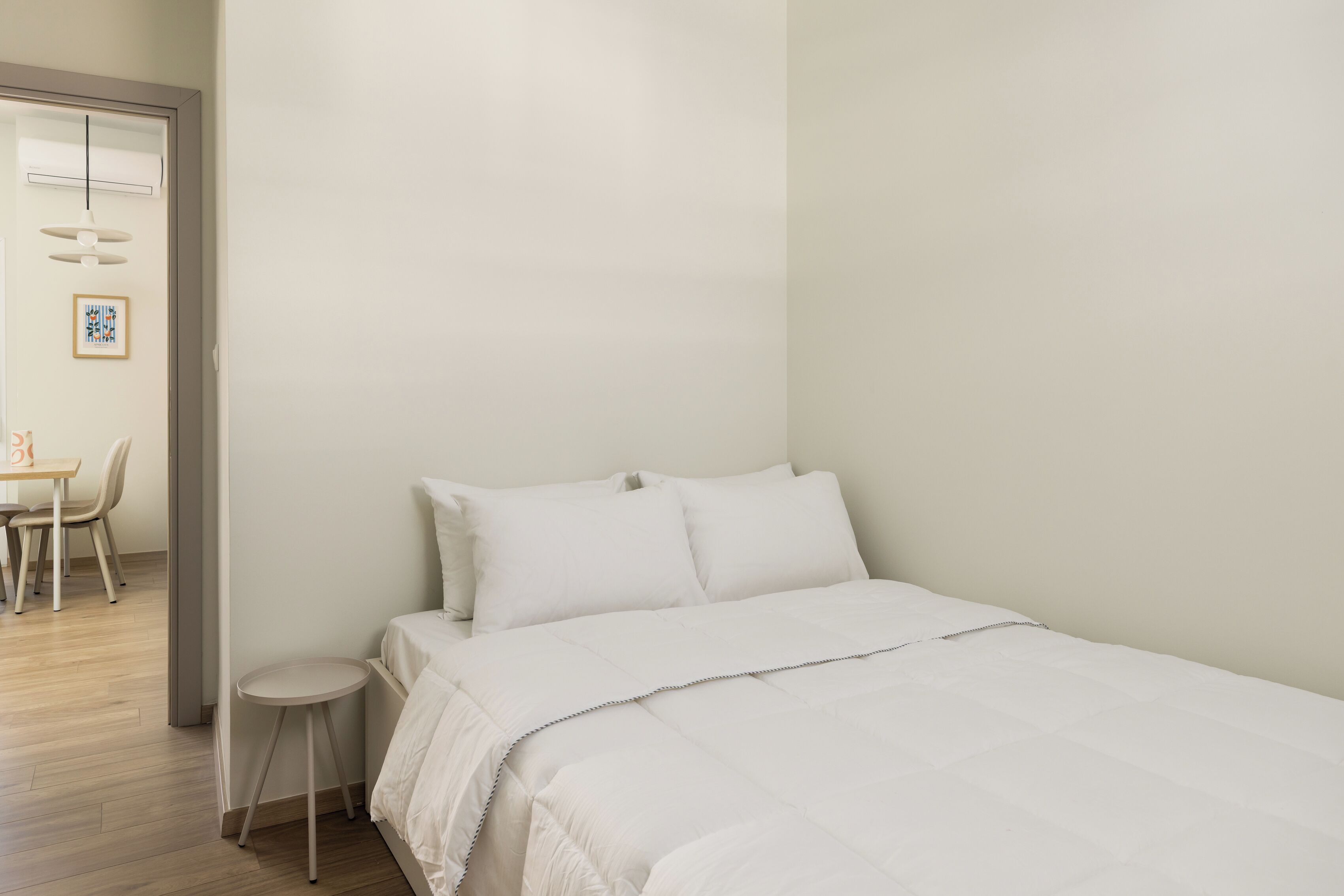 Un dormitorio minimalista con una cama, un taburete pequeño y un escritorio con sillas.
