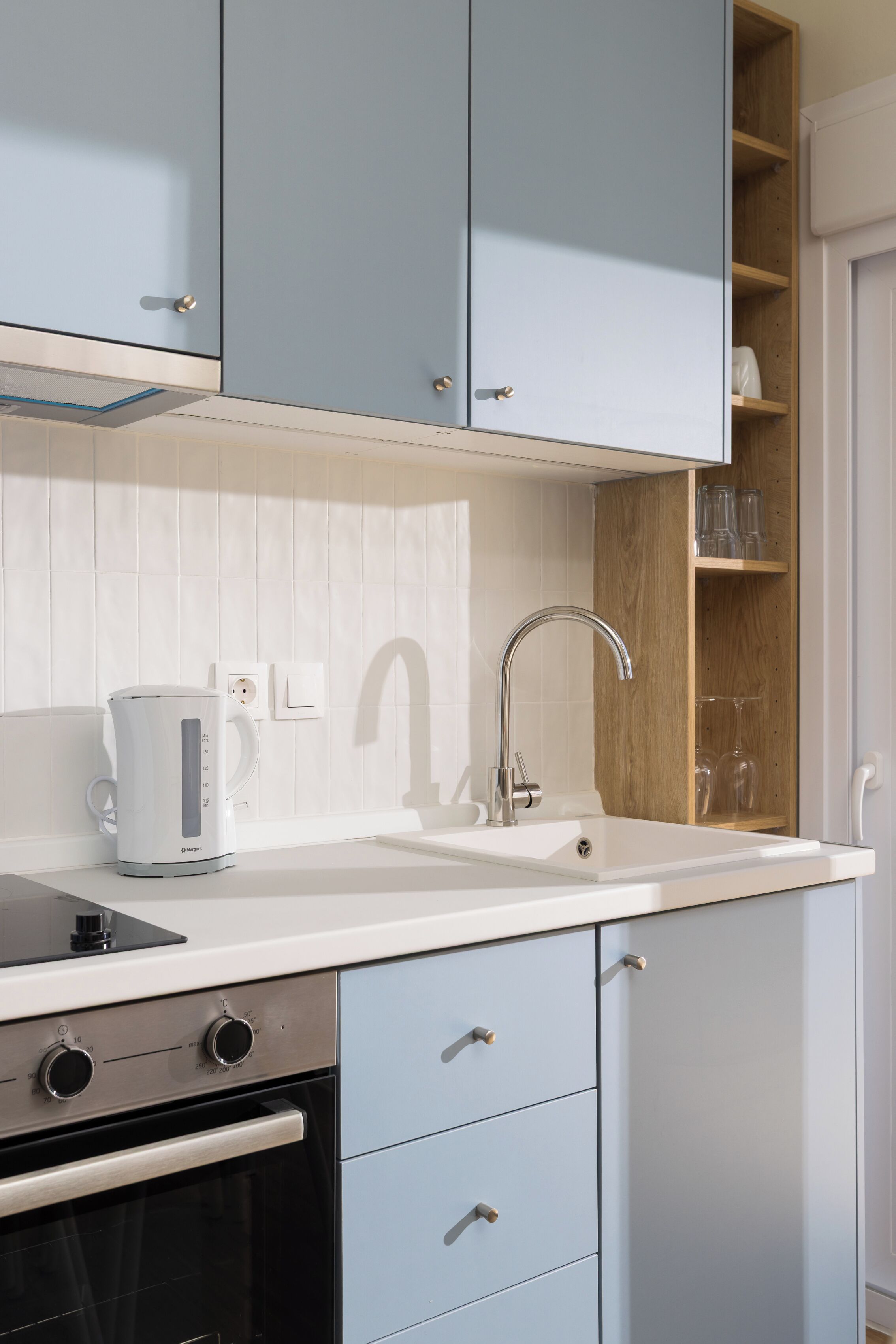 A modern kitchen with light blue cabinets, a white countertop, a built-in oven, a kettle, and a sink.