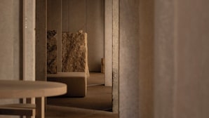 Ein schlichtes Interieur mit einer Betonwand, einer Wand mit Marmoroptik und einem einfachen Holztisch.