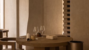 Ein schlichter Essbereich mit einem runden Holztisch, zwei Stühlen und einer Wand mit geometrischem Muster.