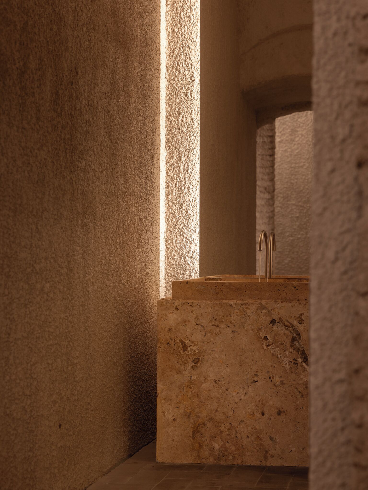 A narrow, dimly lit corridor with rough-textured walls and a marble counter with a sink.