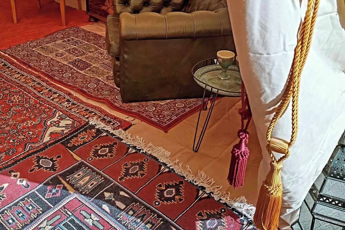 A tented room with a brown sofa, patterned rugs, a small round table, and a chair.