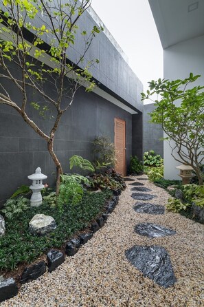 A modern building with a concrete exterior, a gravel pathway, and various plants and garden elements.