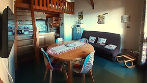 Un salon chaleureux avec une table à manger en bois, un canapé et un coin cuisine équipé d’un four à micro-ondes et de placards.