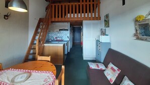 Une pièce chaleureuse avec un escalier en bois, un coin repas, une cuisine et un espace de vie comprenant un canapé et des coussins.