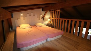 Une chambre dans une cabane en bois, avec deux lits, un plafond en bois et une table de chevet avec une lampe.