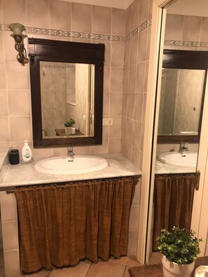 Ein Badezimmer mit einem weißen Waschbecken, einem großen Spiegel und einer durch eine Glastür sichtbaren Dusche.