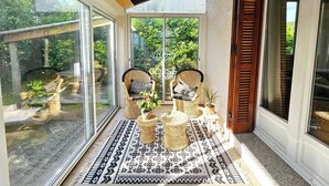 A sunlit patio with wicker furniture, a patterned rug, and a view of greenery through large glass doors. - Villa Lina 5 pers beaches and rivers (Prunelli-di-Fiumorbo)