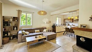 A modern living room with a sofa, coffee table, and a kitchen area with a dining table and chairs. - Villa Lina 5 pers beaches and rivers (Prunelli-di-Fiumorbo)