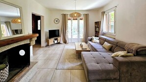 A spacious living room with a large sofa, a coffee table, and a fireplace. There is a television and a clock on the wall. - Villa Lina 5 pers beaches and rivers (Prunelli-di-Fiumorbo)