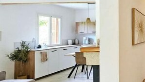 A modern kitchen with white cabinets, a wooden countertop, and a dining area with a table and chairs. - Villa Lina 5 pers beaches and rivers (Prunelli-di-Fiumorbo)