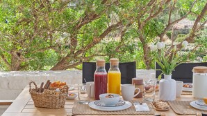An outdoor dining table set with breakfast items, including bread, a basket, and a variety of drinks.
